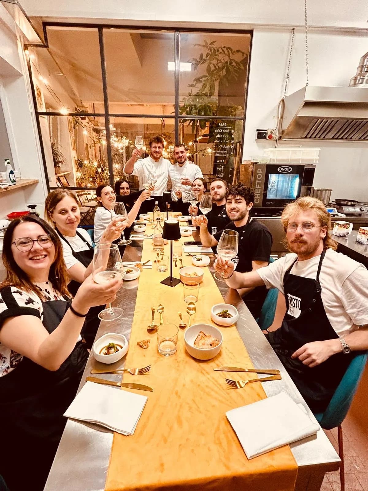 Un gruppo a tavola brinda sorridendo, con gli chef in piedi in fondo alla sala