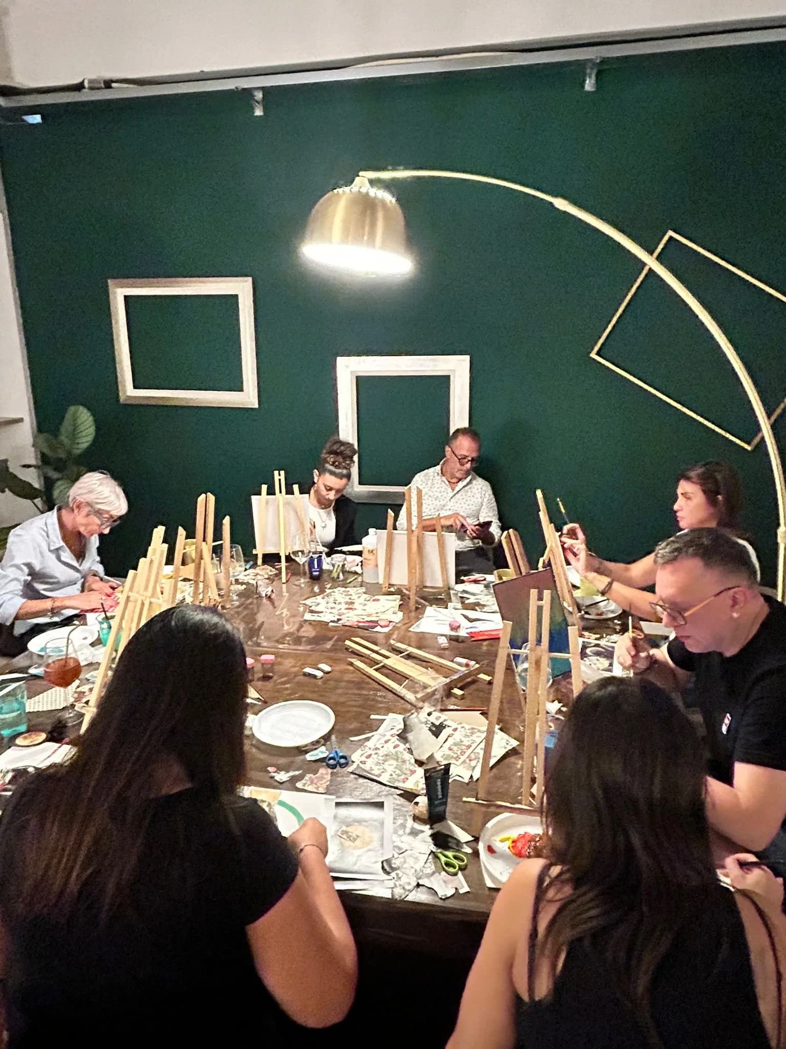 Un gruppo dipinge su piccole tele attorno a un grande tavolo, in una sala dalle pareti verdi