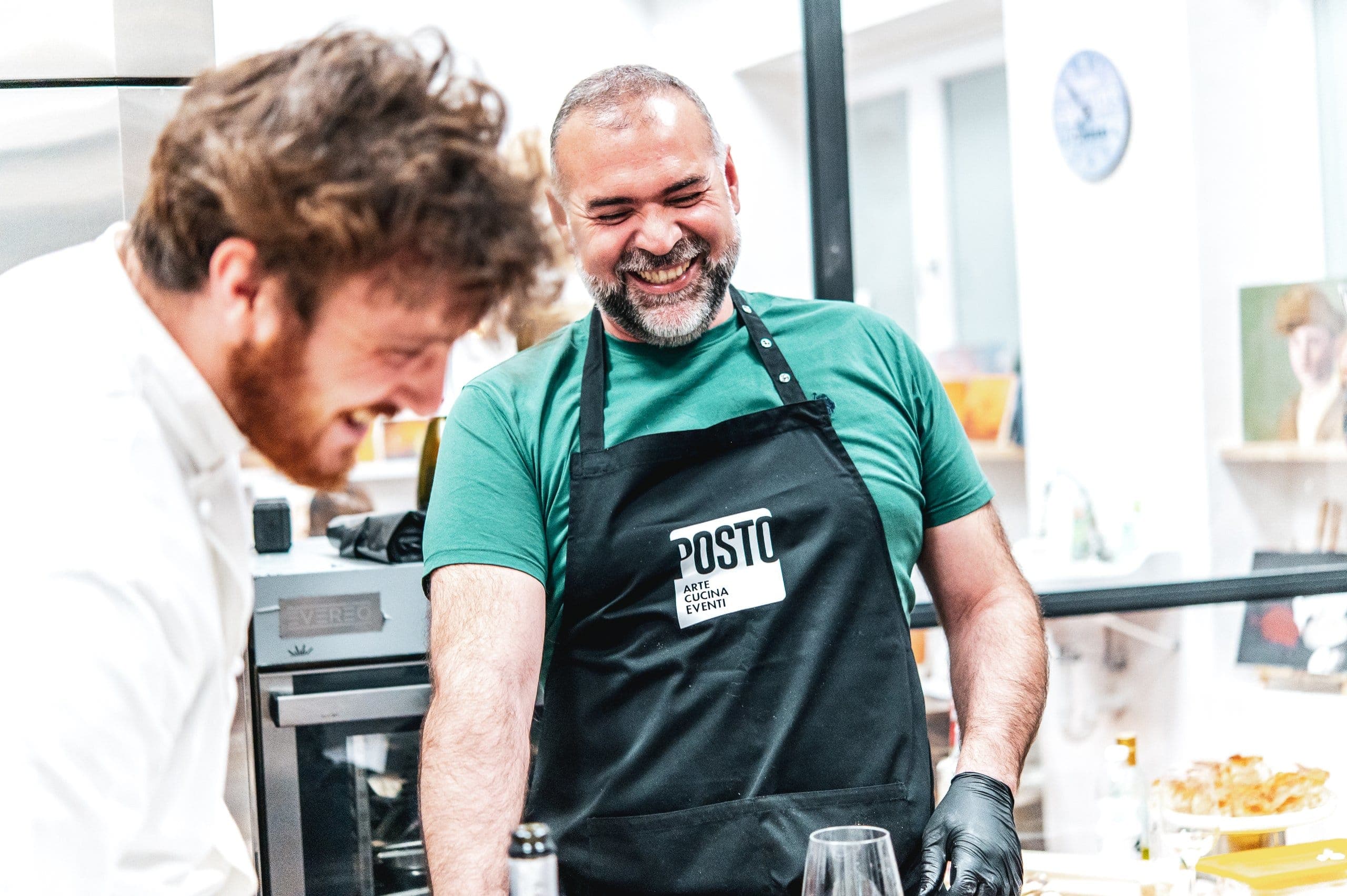 Uno chef e un partecipante col grembiule di POSTO ridono ai fornelli