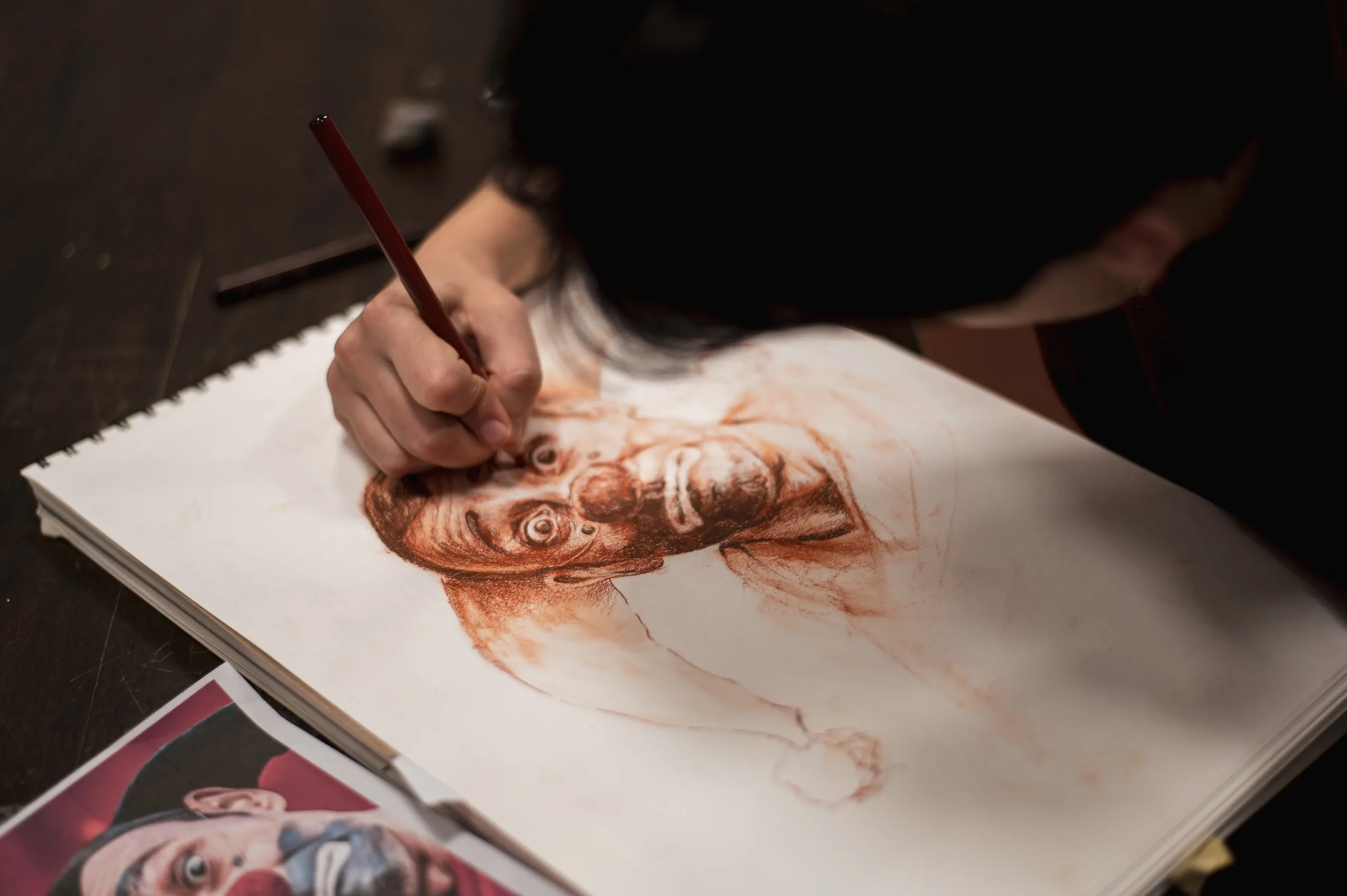 Una mano disegna a sanguigna un volto femminile su carta