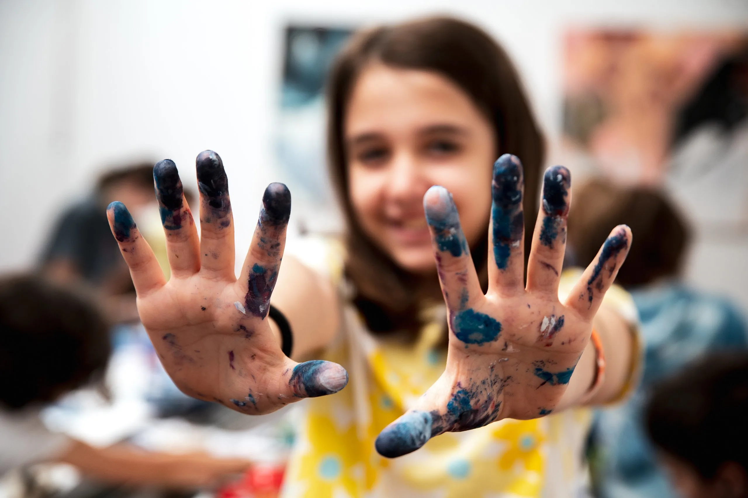 Una bambina sorride e mostra le mani sporche di colore blu