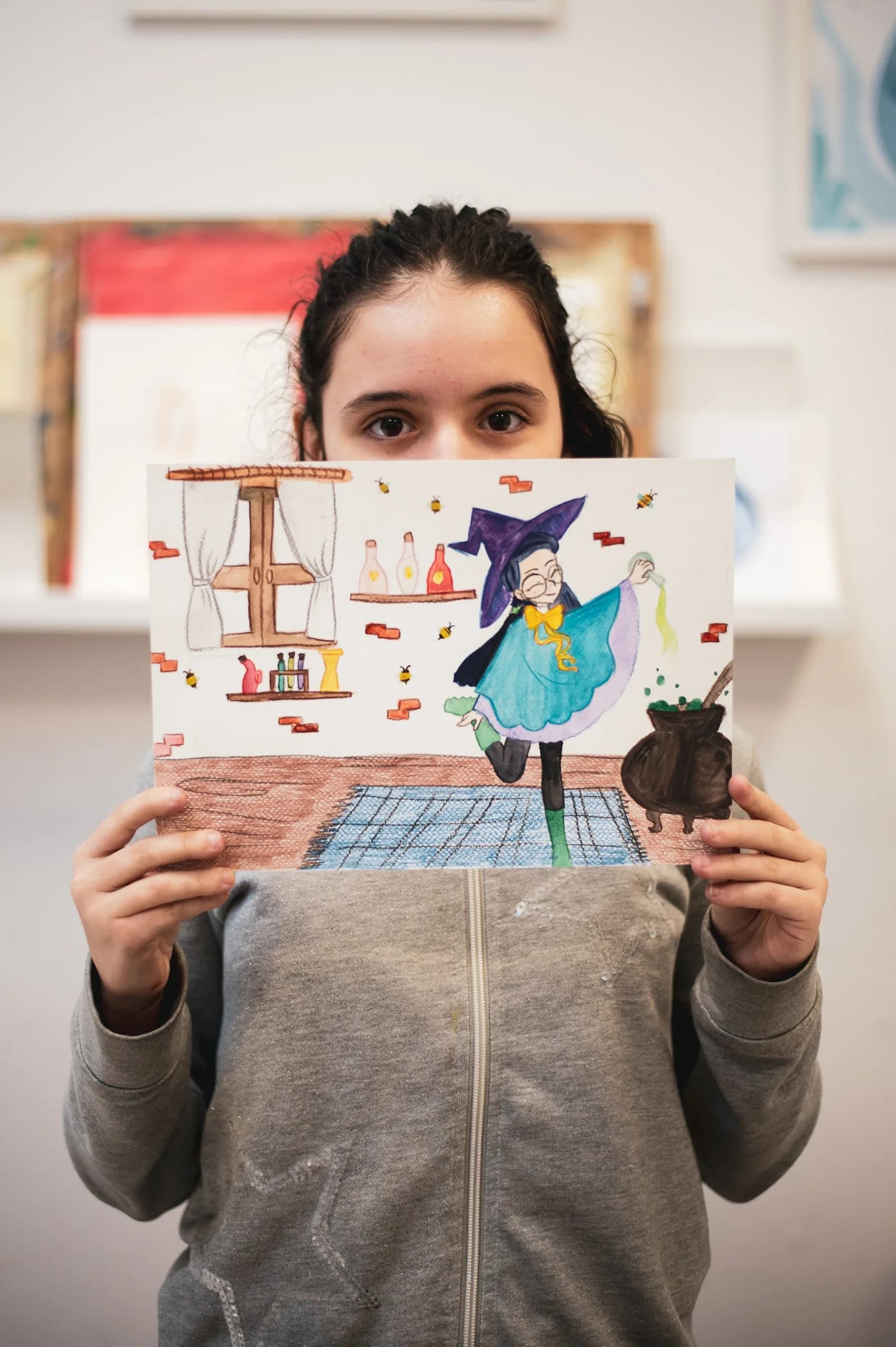 Una ragazza tiene davanti a se' il suo disegno di una strega in cucina