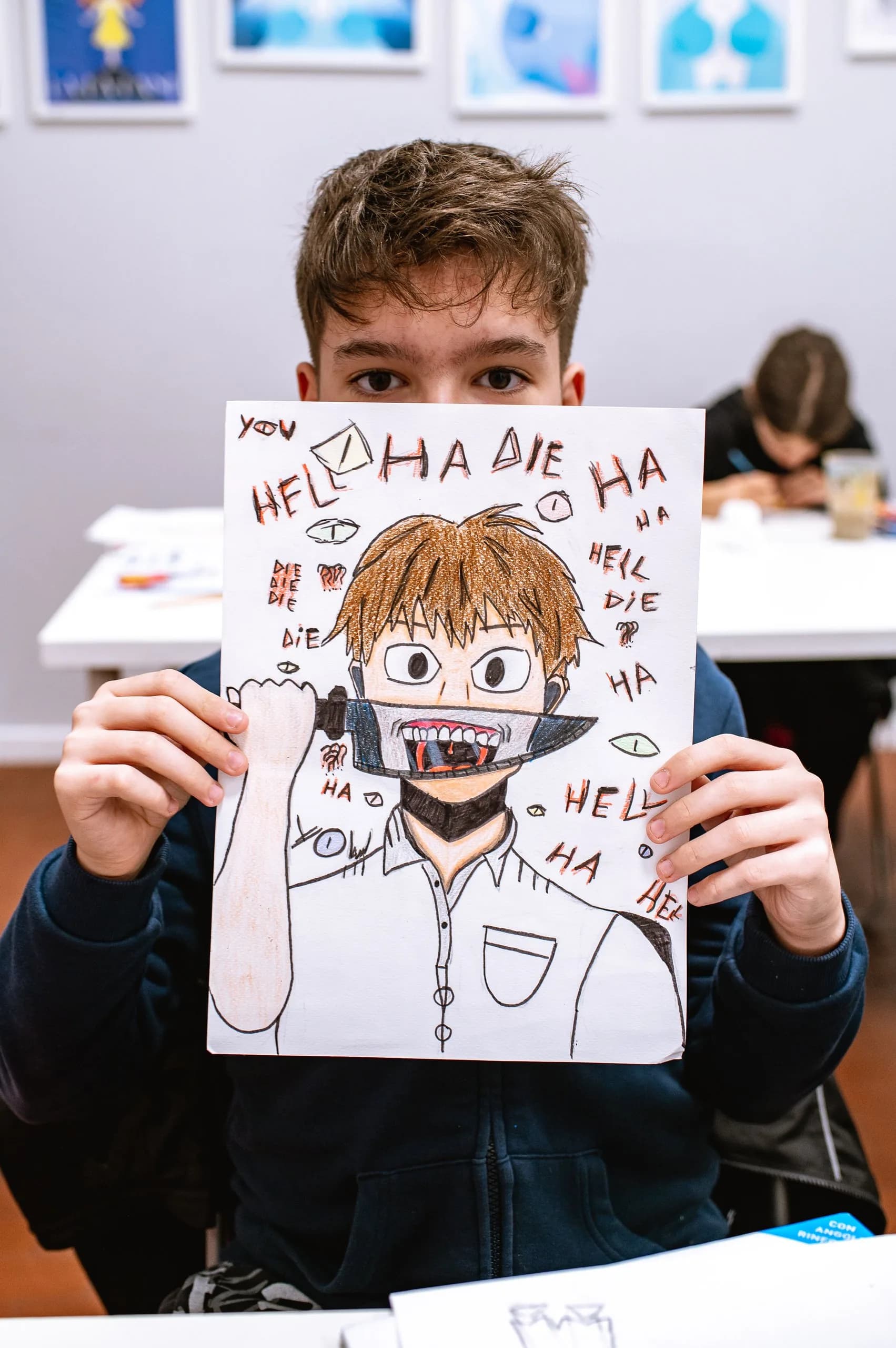 Un ragazzo tiene davanti al viso il suo disegno a pennarello di un personaggio
