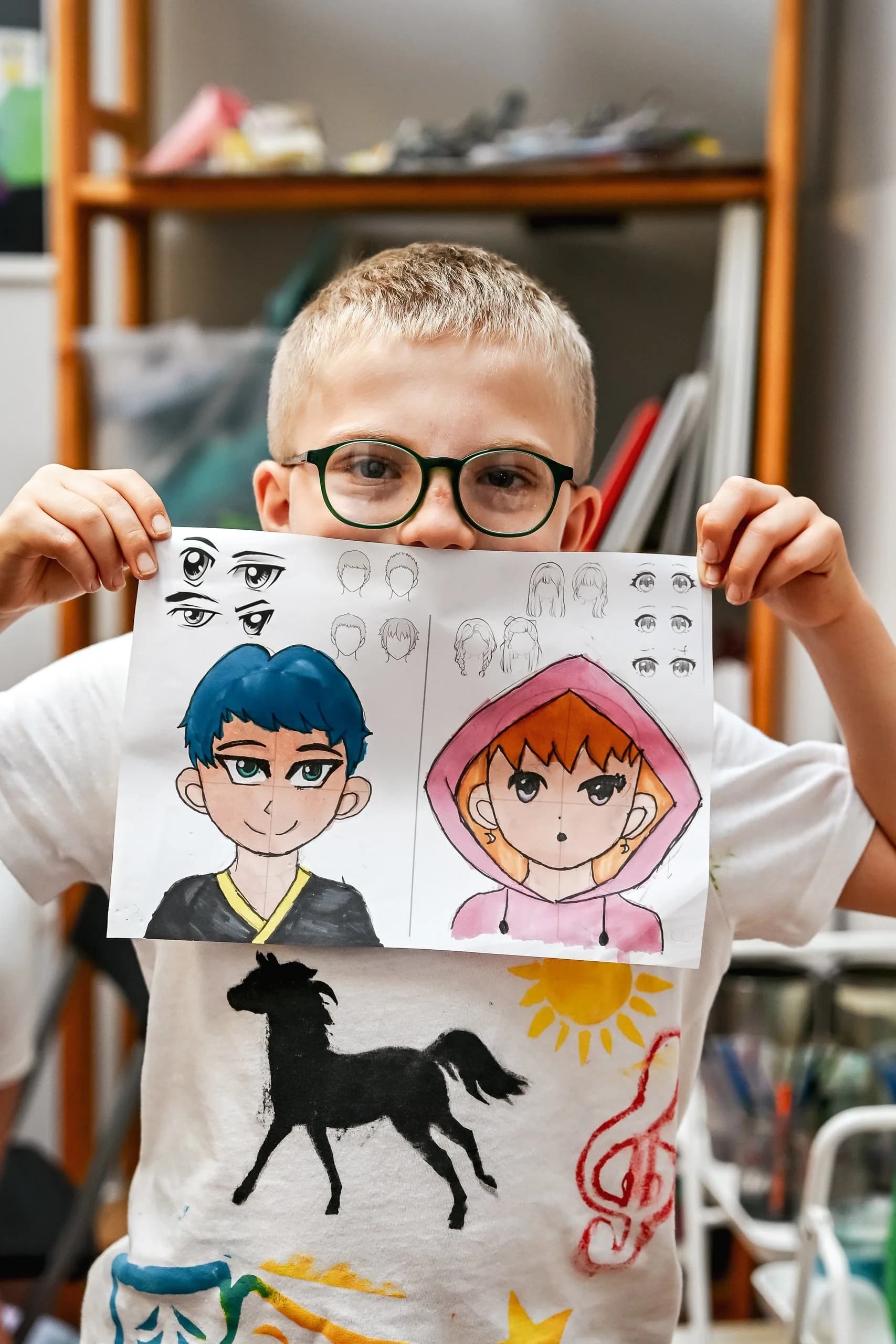 Un bambino con gli occhiali mostra i suoi volti disegnati in stile manga